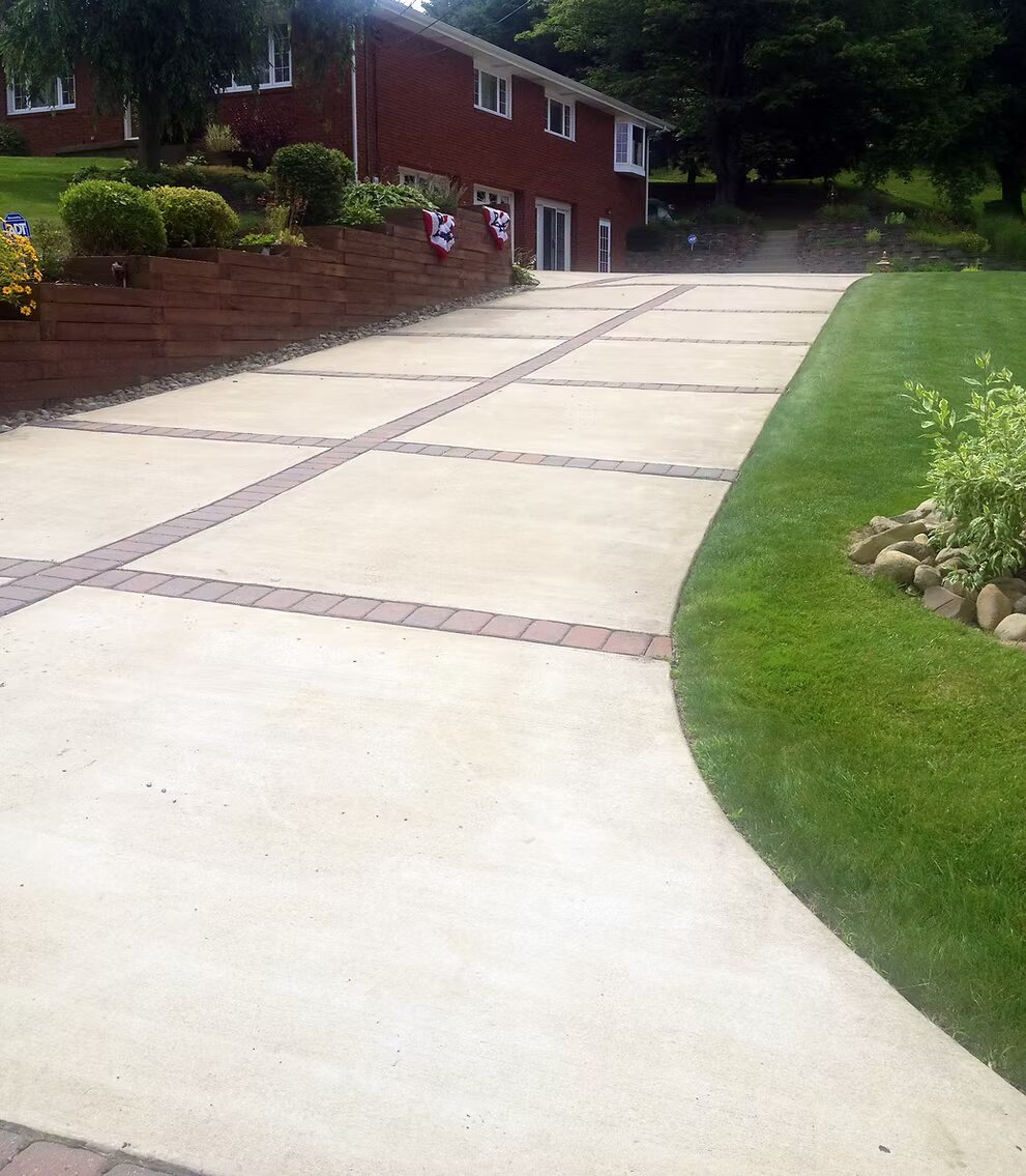 Wide concrete driveway with decorative brick paver grid pattern at a brick colonial home