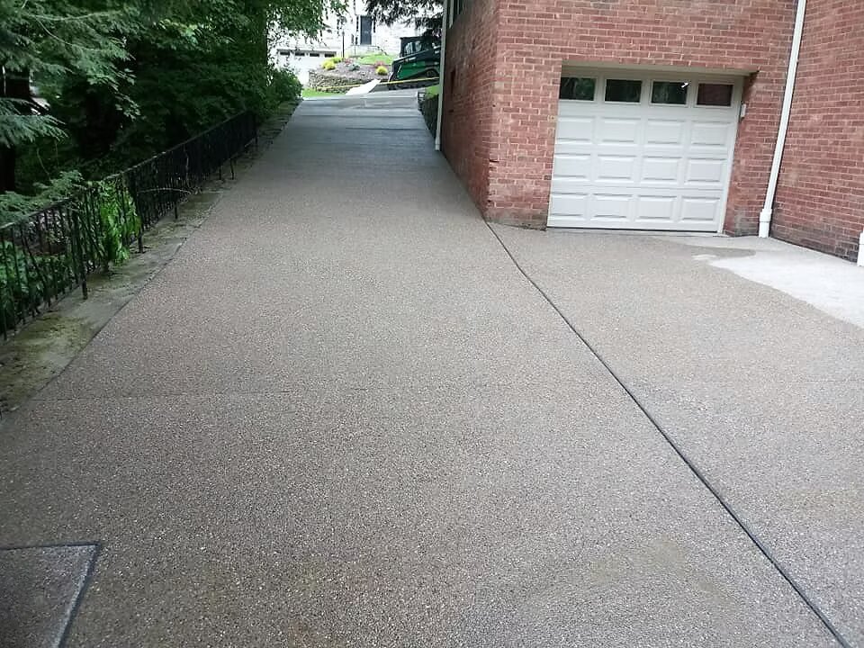 Exposed aggregate concrete driveway with textured finish leading to a brick home garage