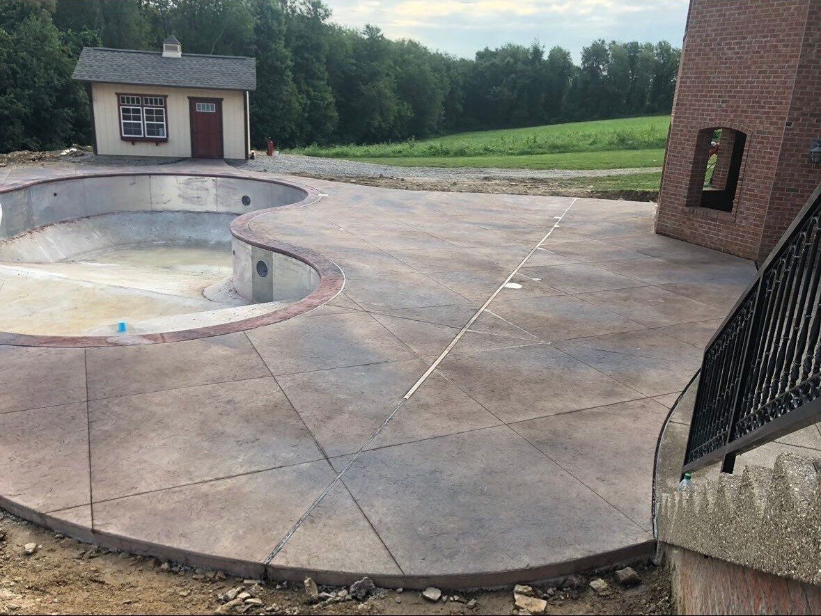 Wide stamped concrete pool deck with decorative crimson border around a freeform pool shell