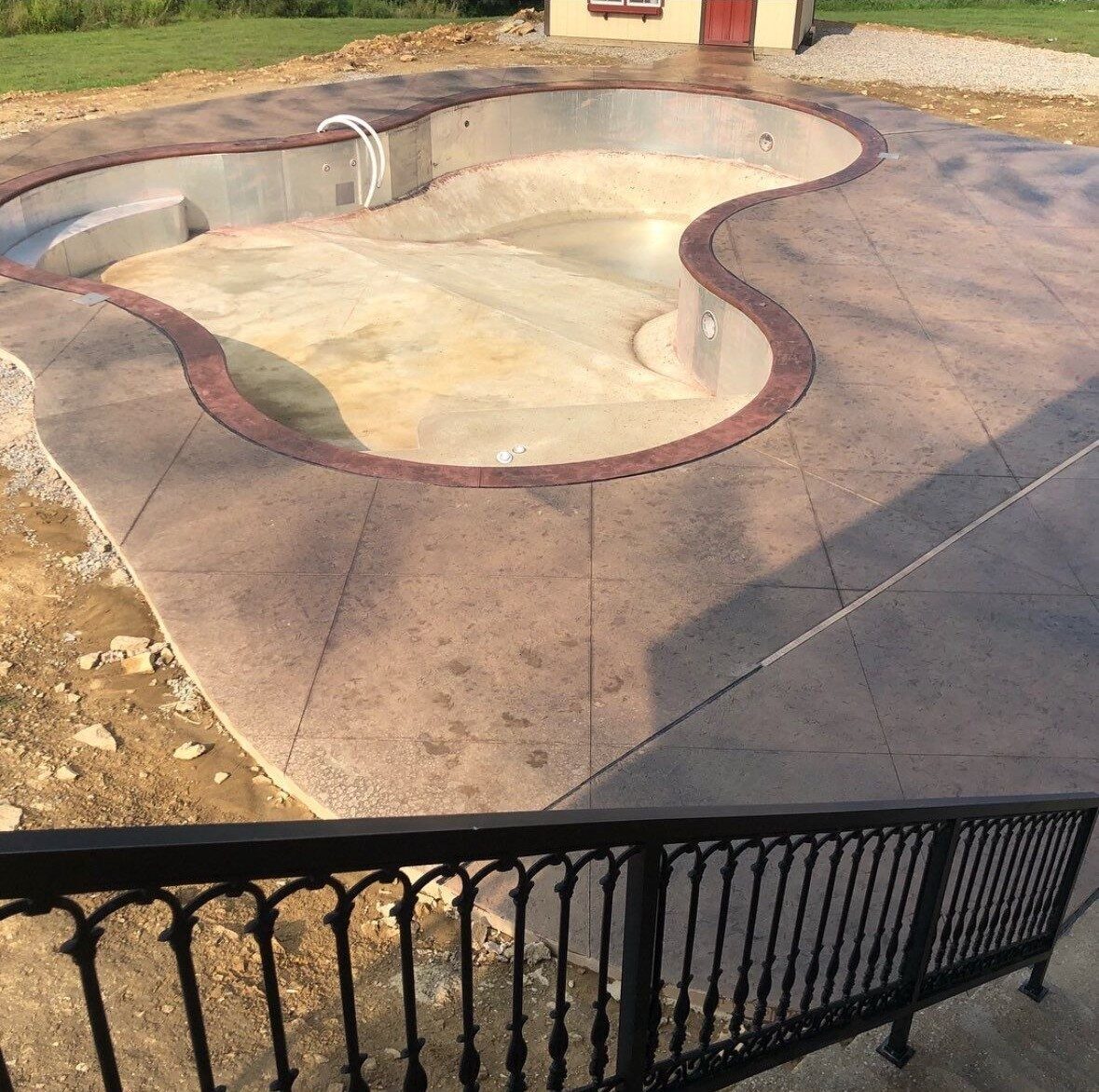 Aerial view of stamped concrete pool deck surrounding a freeform pool with iron railing