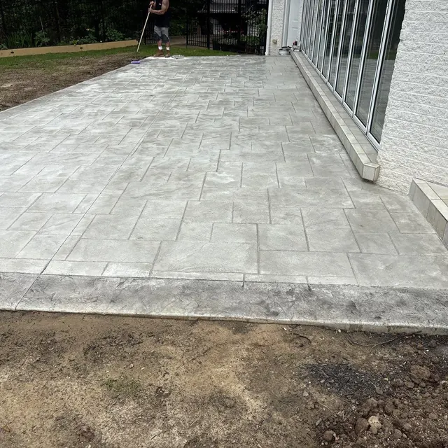 Light gray stamped concrete patio with a large rectangular stone pattern beside a home