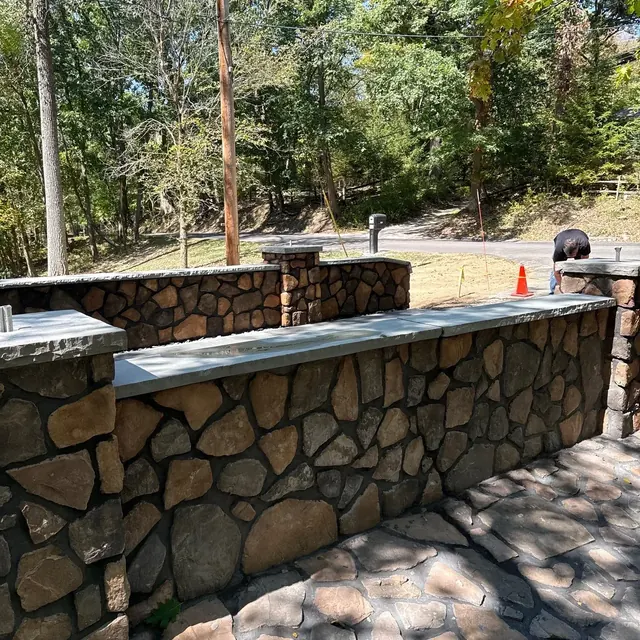 Natural stone-faced retaining wall with a concrete cap beside a stone patio