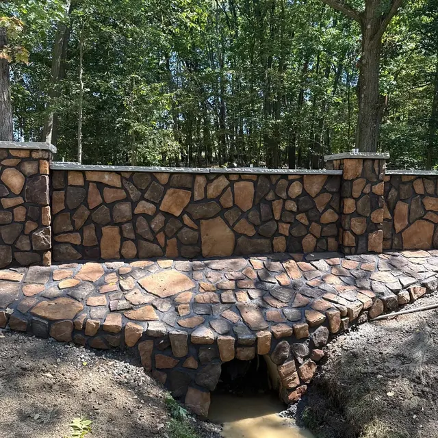 Natural stone-faced retaining wall and stone culvert crossing in a wooded yard