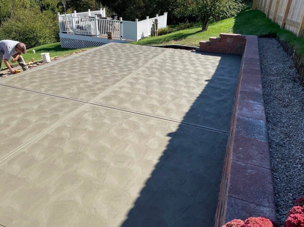 Freshly finished stamped patio with brick block retaining wall along the property edge
