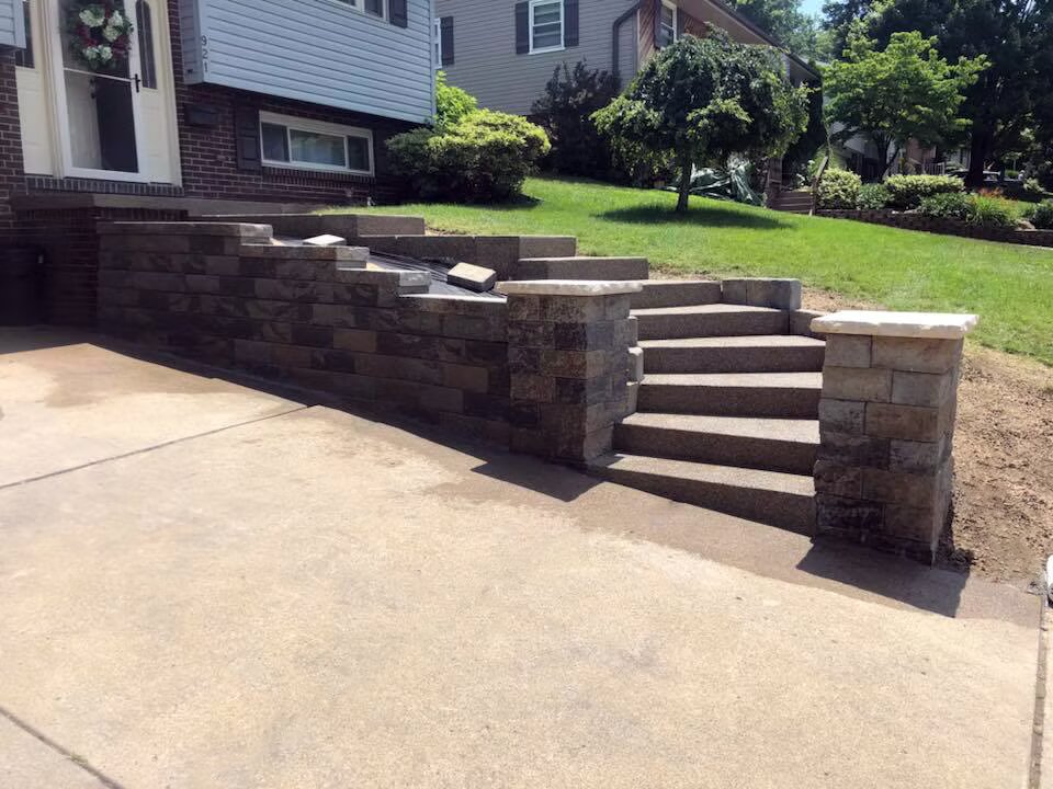 Block retaining wall with concrete steps and pillar caps at the front of a brick home