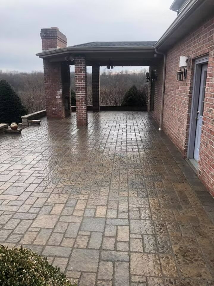 Stamped cobblestone-pattern concrete patio at a covered outdoor area of a brick home